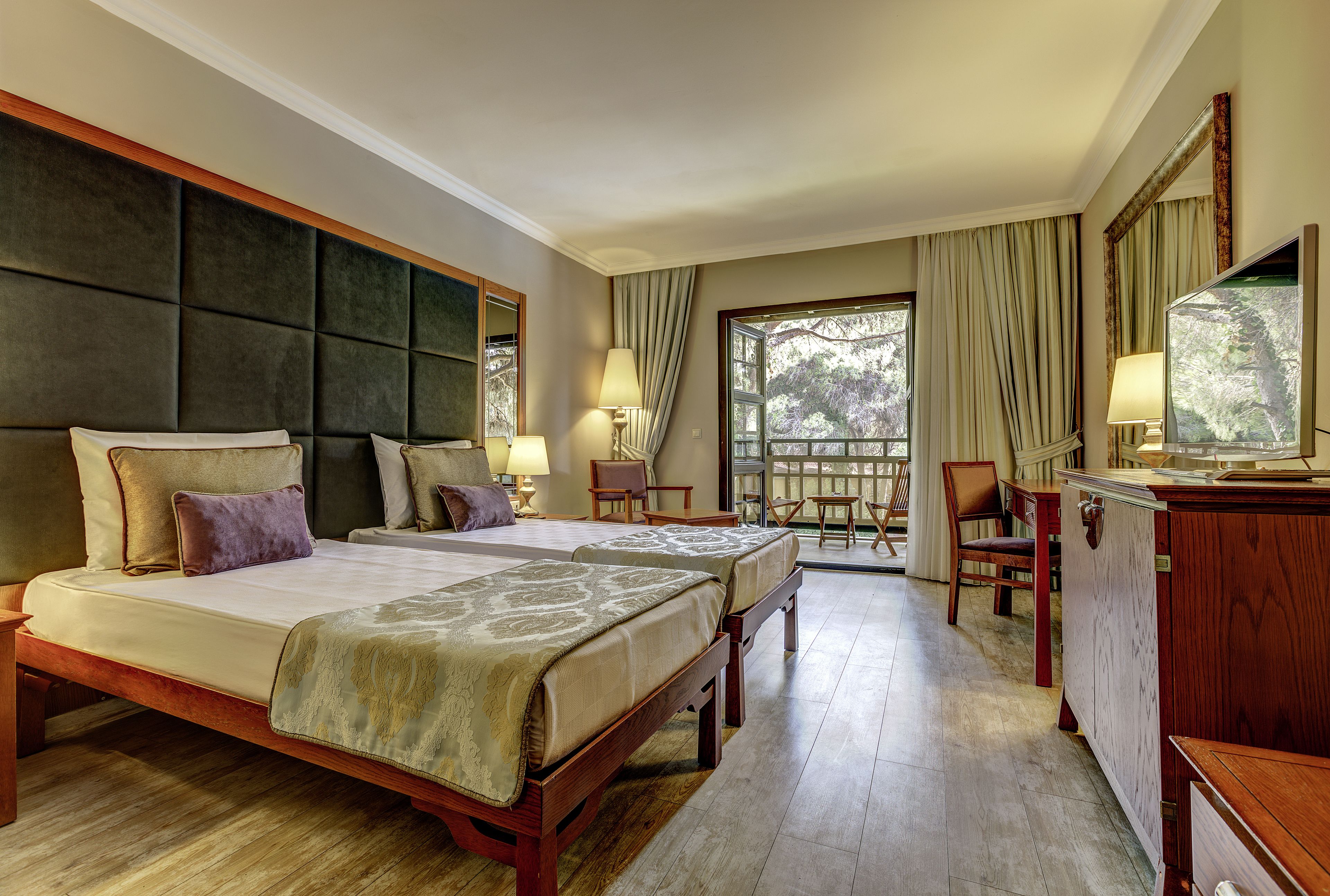 A hotel room with two beds, a desk, a chair, and a view of the outdoors.