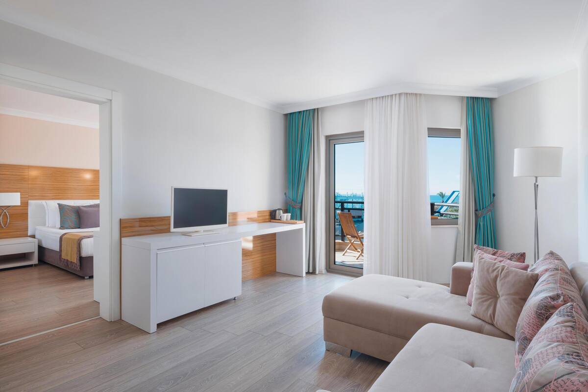 A modern hotel room with a flat-screen TV, a sofa, a desk, and a balcony with a view.