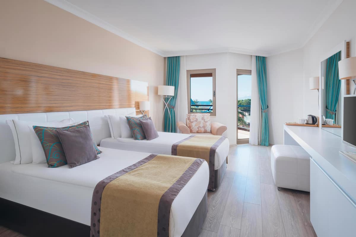 A hotel room with two beds, a sofa, a desk, and a view of the sea.