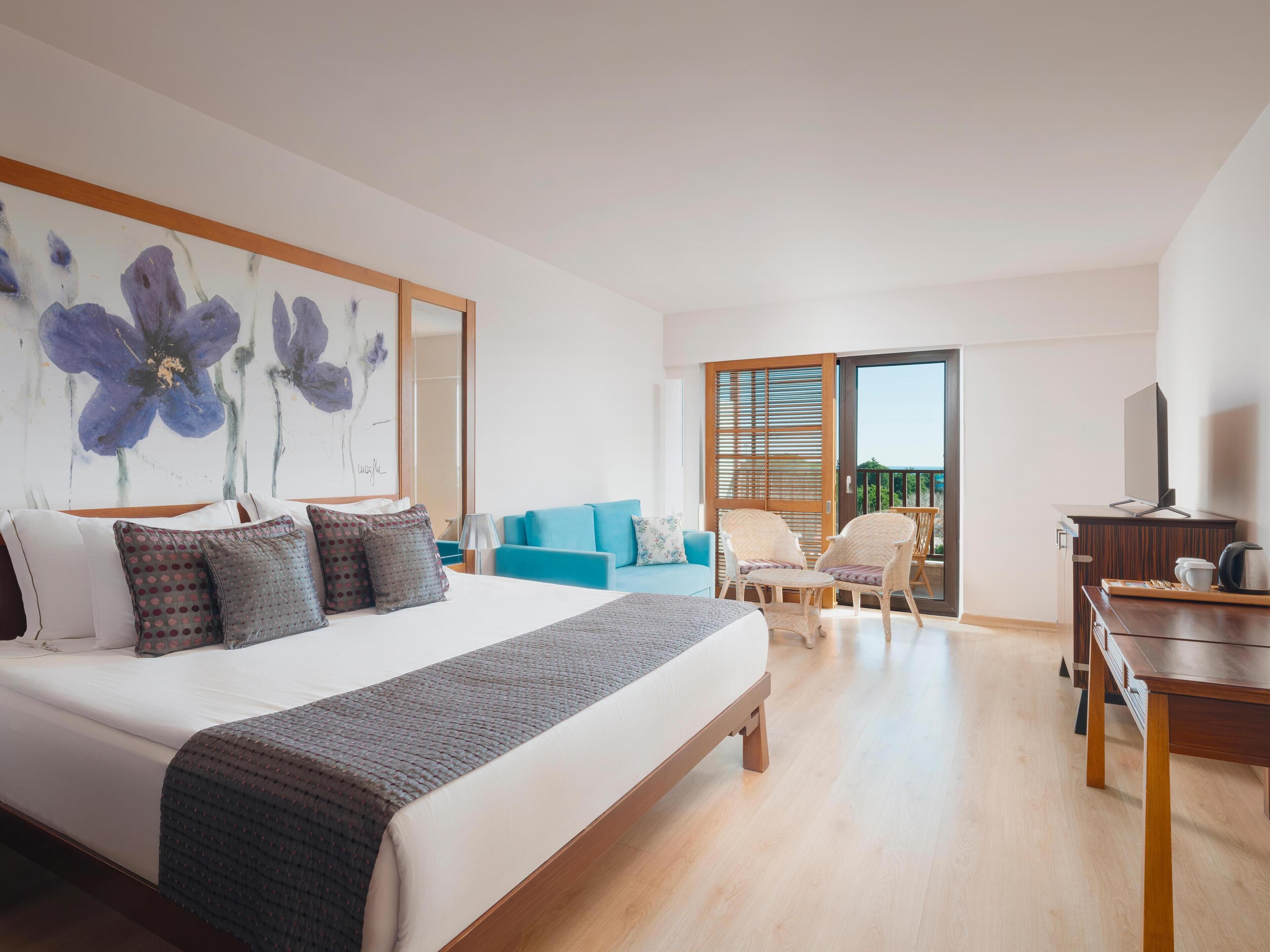 A modern hotel room with a large bed, a blue sofa, a wooden desk, and a balcony with a view.