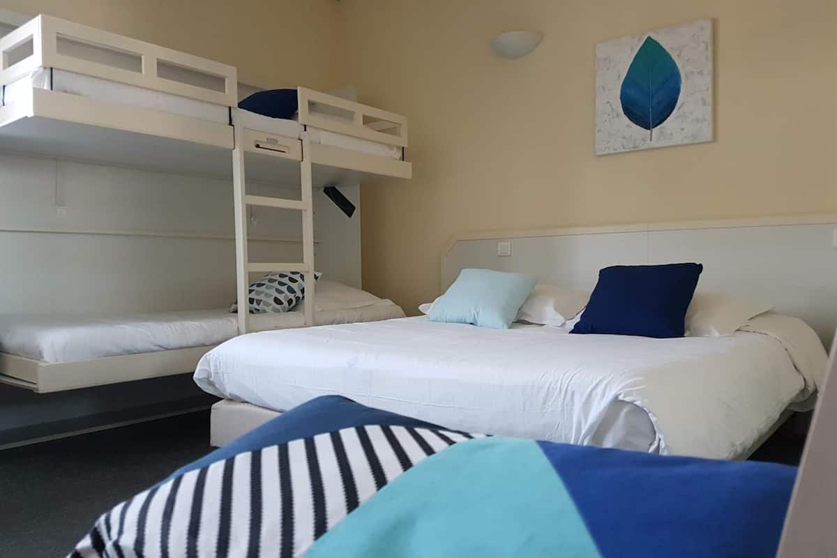 A room with bunk beds, a bed with pillows, and a wall with a leaf painting.