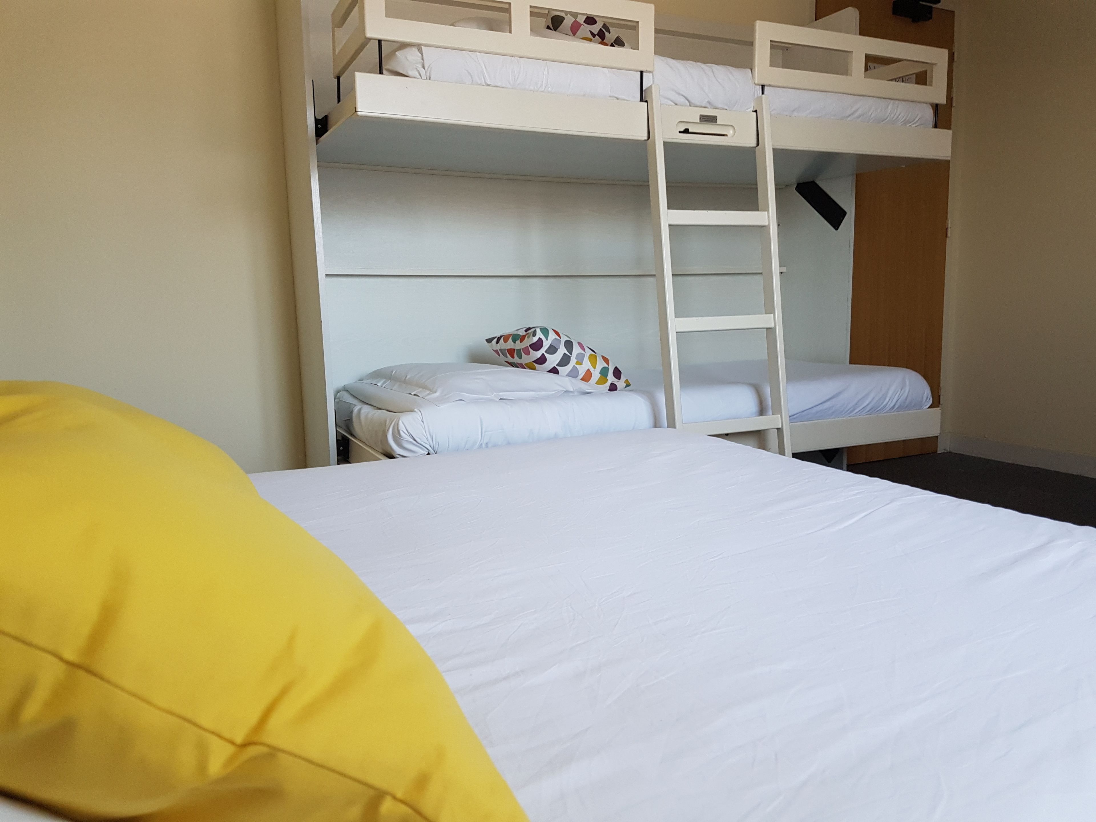 A bunk bed room with a ladder, a bed with a yellow pillow, and a white mattress.