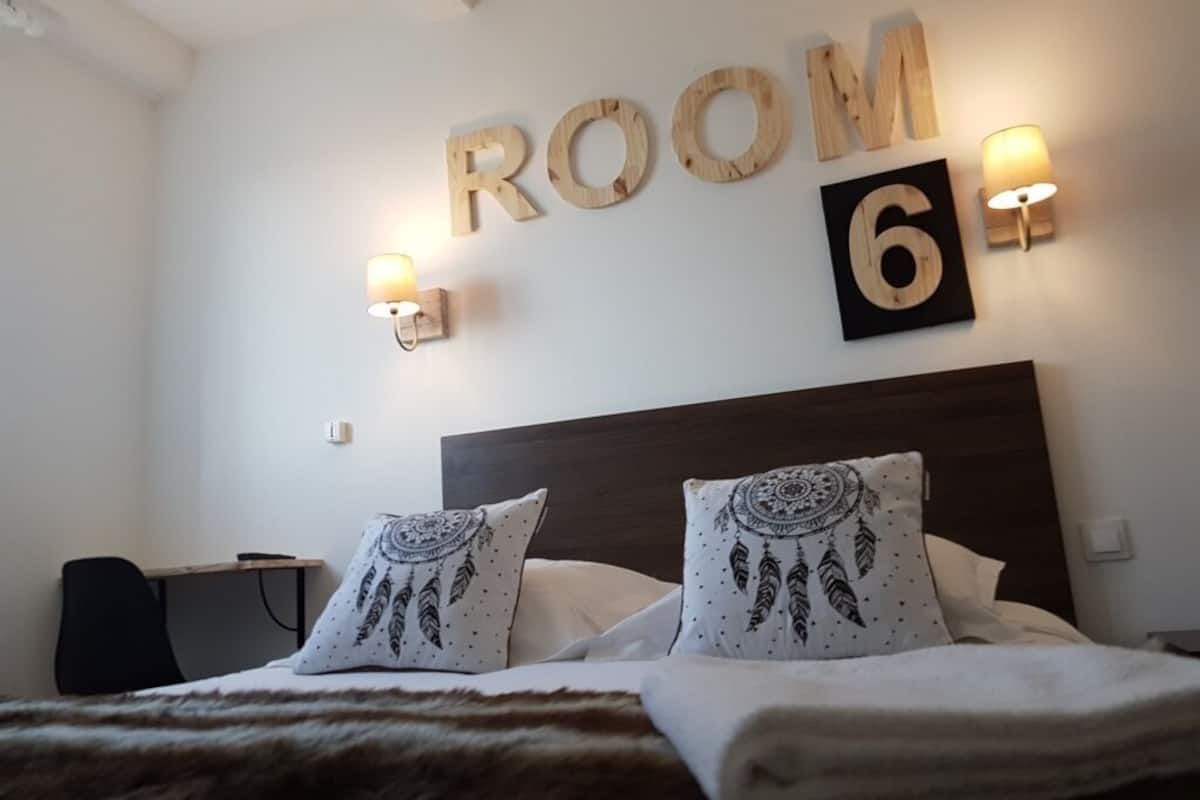 A bedroom with a bed, pillows, a headboard, and a wall sign indicating "ROOM 6".