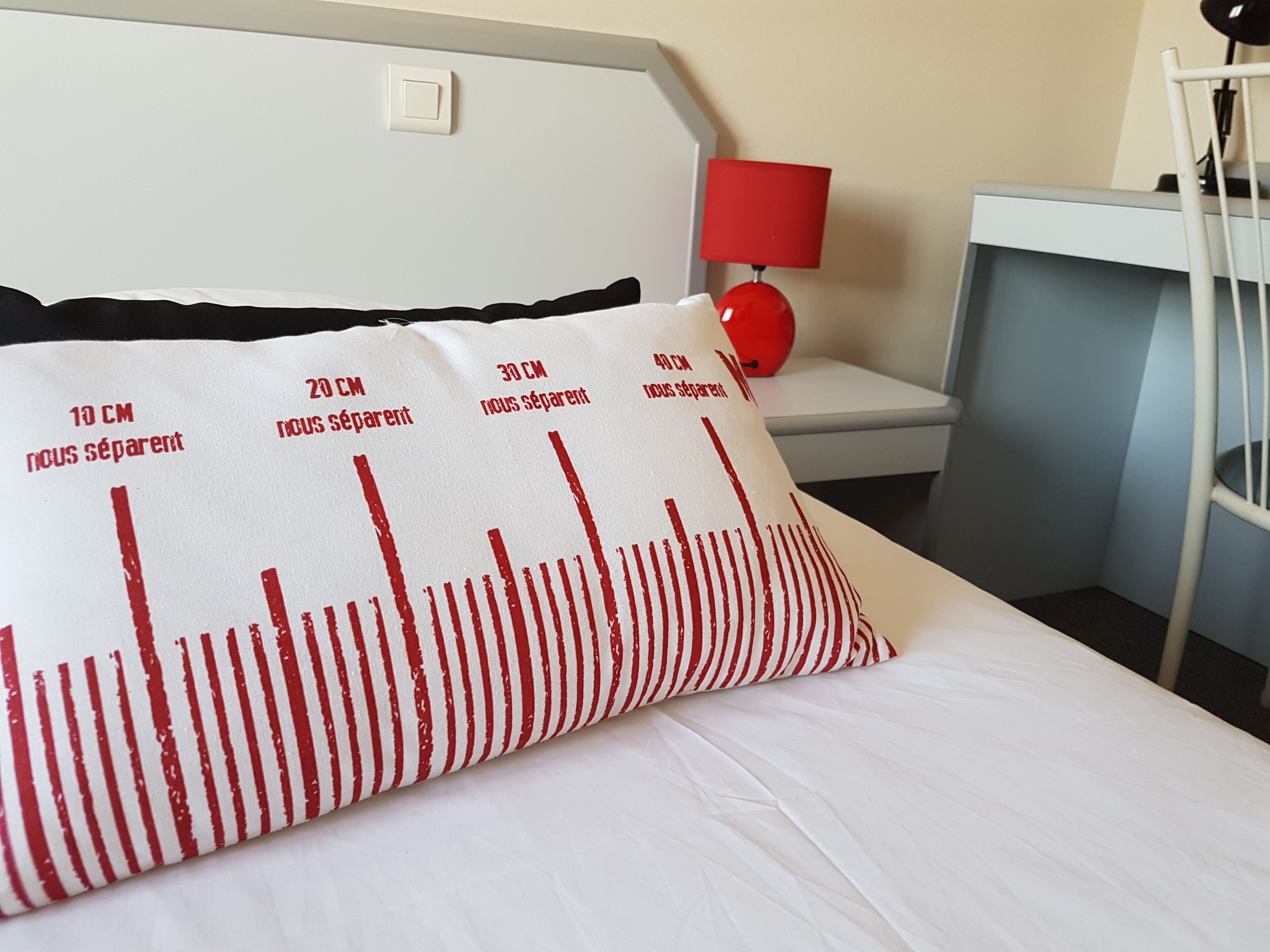 Une chambre d’hôtel avec un lit doté d’un oreiller sur lequel figure, en lettres rouges, les dimensions.