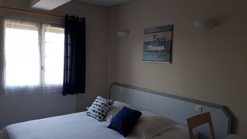 A bedroom with a bed, a window with curtains, a wall-mounted light, and a sign.