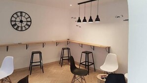 A modern interior with a wooden bar counter, black stools, a white chair, and a wall clock. - Le Sainte Florence (Essarts en Bocage)