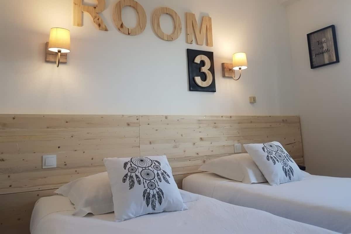 A hotel room with two beds, wooden headboard, wall-mounted number '3', and two wall sconces.