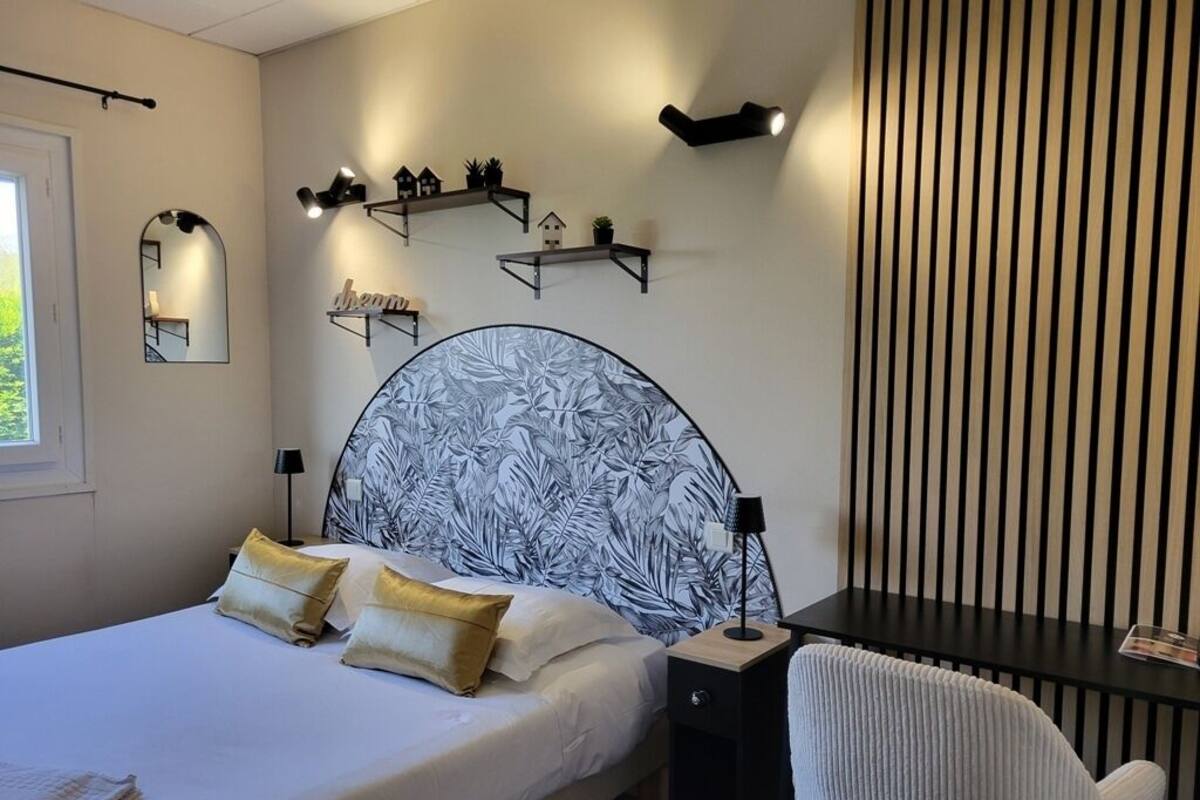 A bedroom with a large bed, bedside tables, a desk, and a chair. There are wall-mounted shelves with decorative items and a mirror.