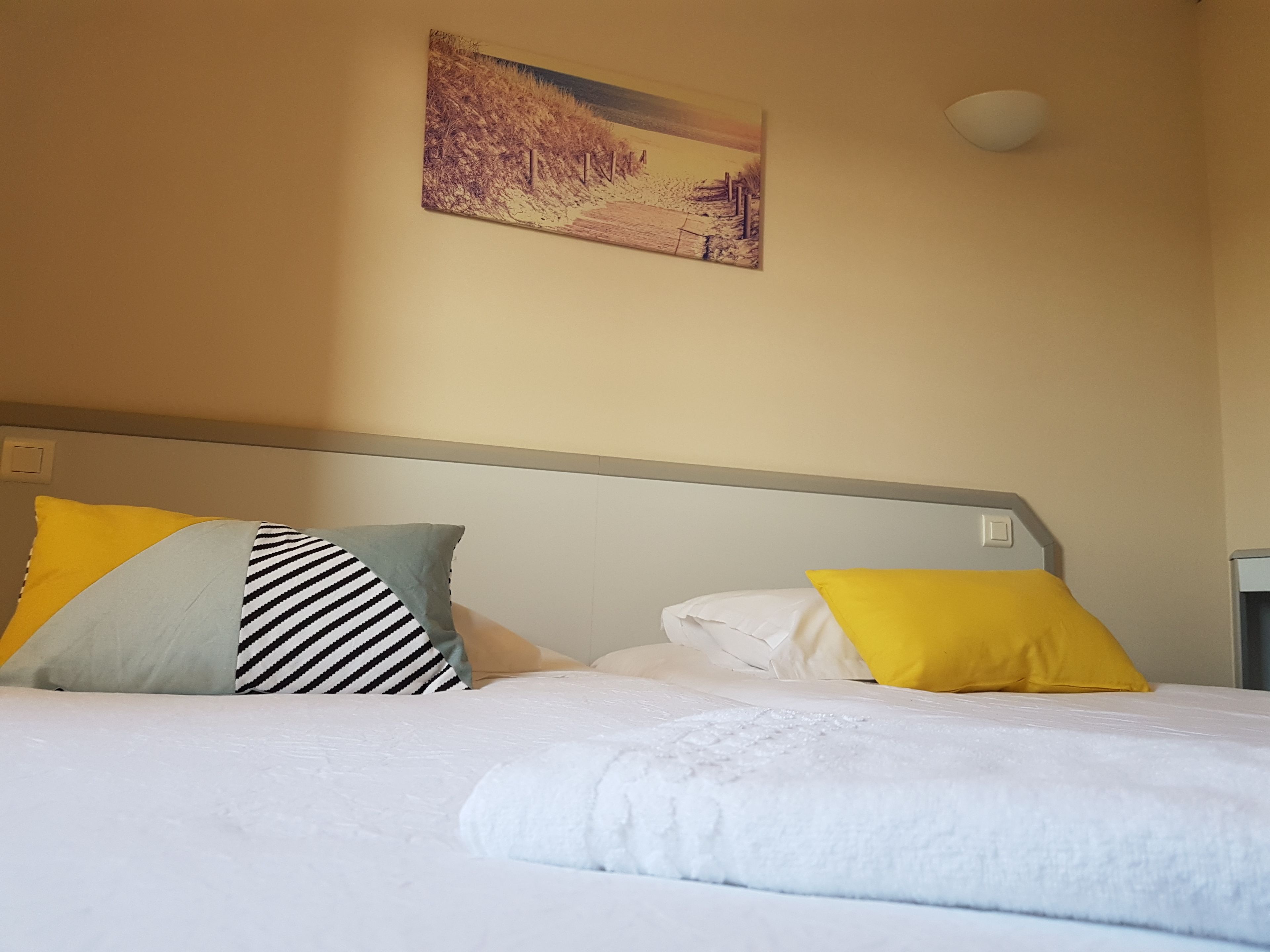 A hotel room with a bed, pillows, a painting on the wall, and a bedside table.