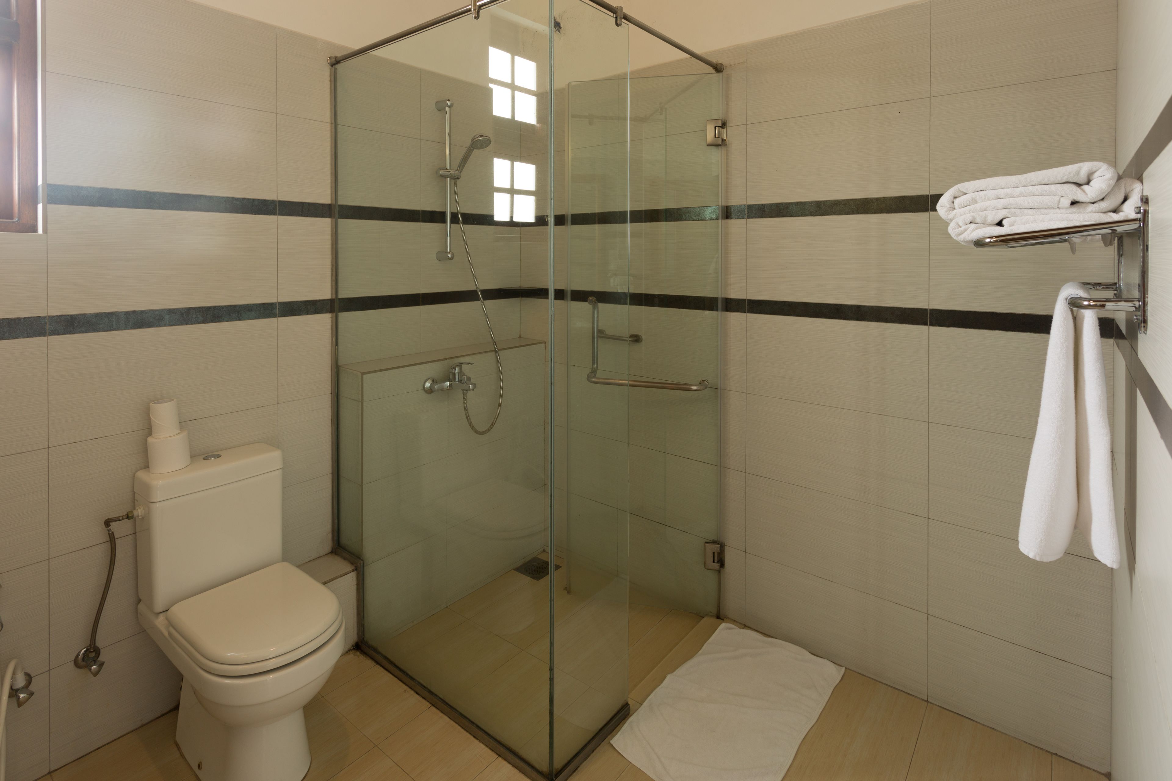 Een moderne badkamer met een douche met glazen wand, een toilet en een handdoekhouder.