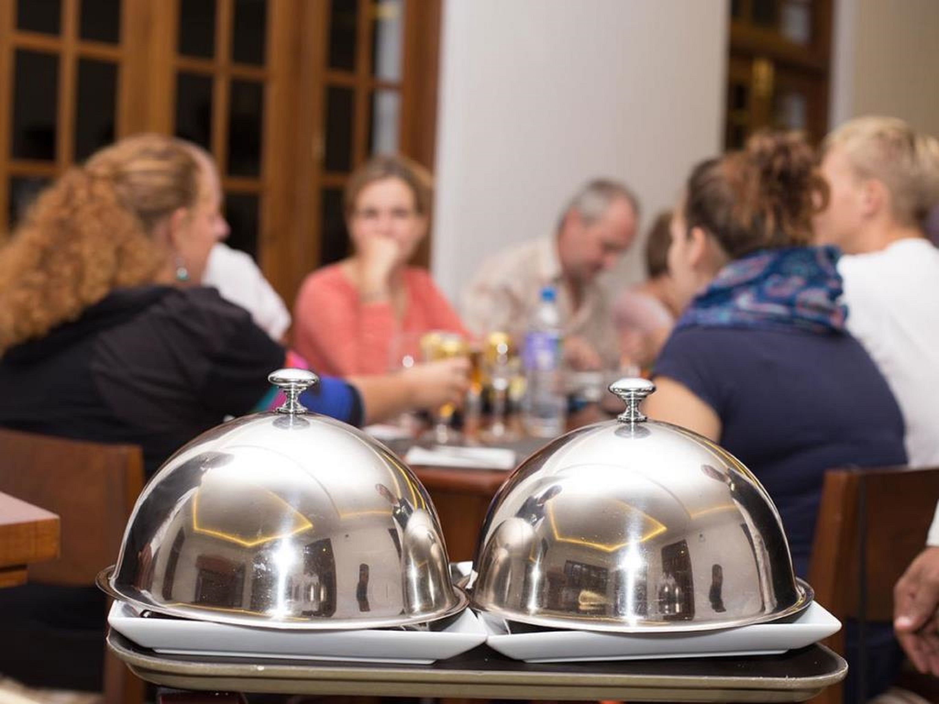 A dining table with two covered silver dishes in the foreground.