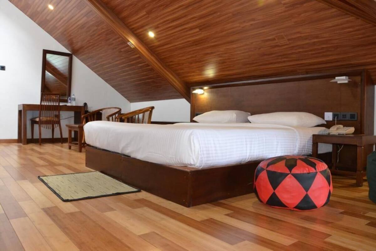 A bedroom with a wooden ceiling, a bed with white bedding, a desk with a chair, and a red and black bean bag.