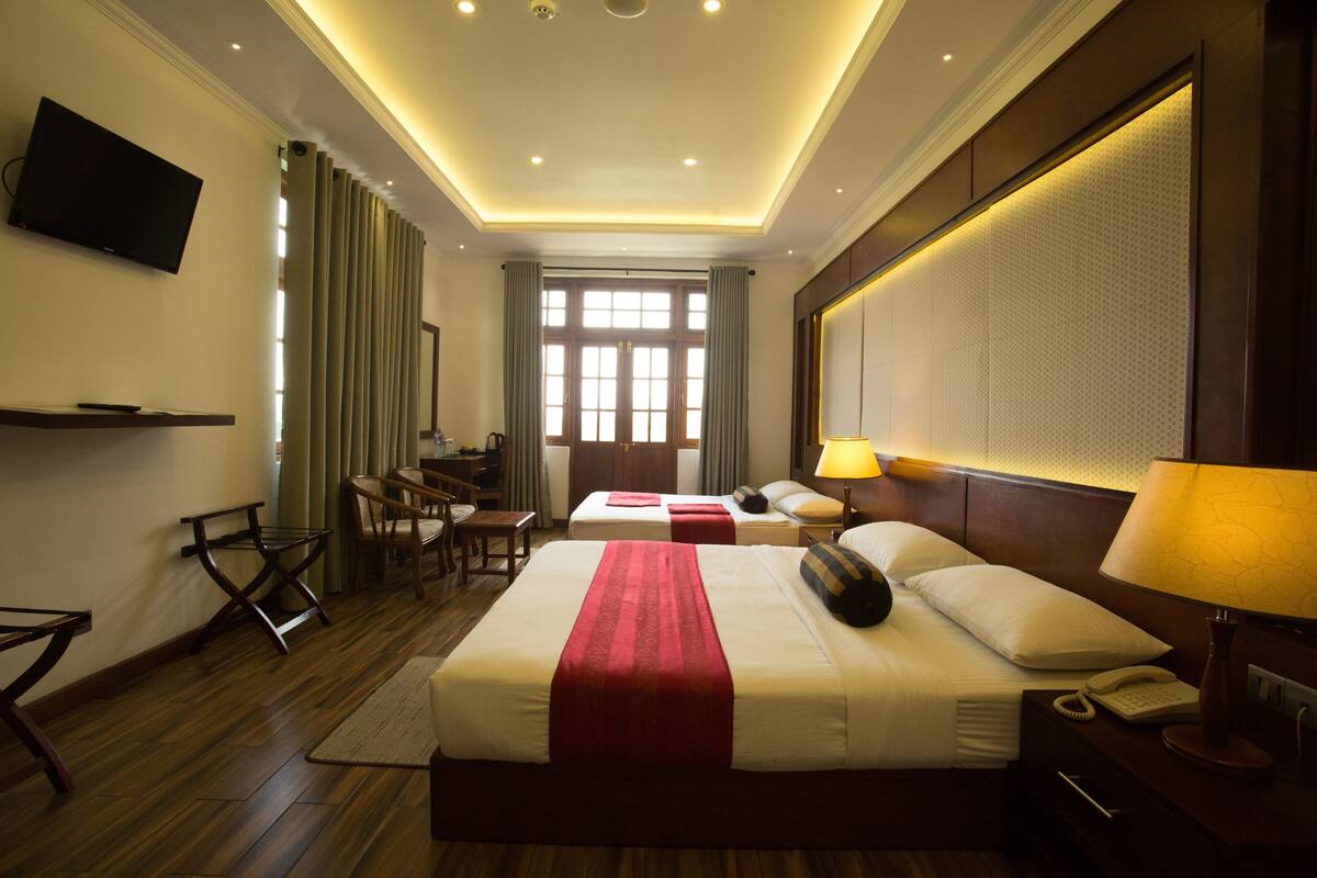 A hotel room with a large bed, bedside tables, a TV, a desk, and a window with curtains.