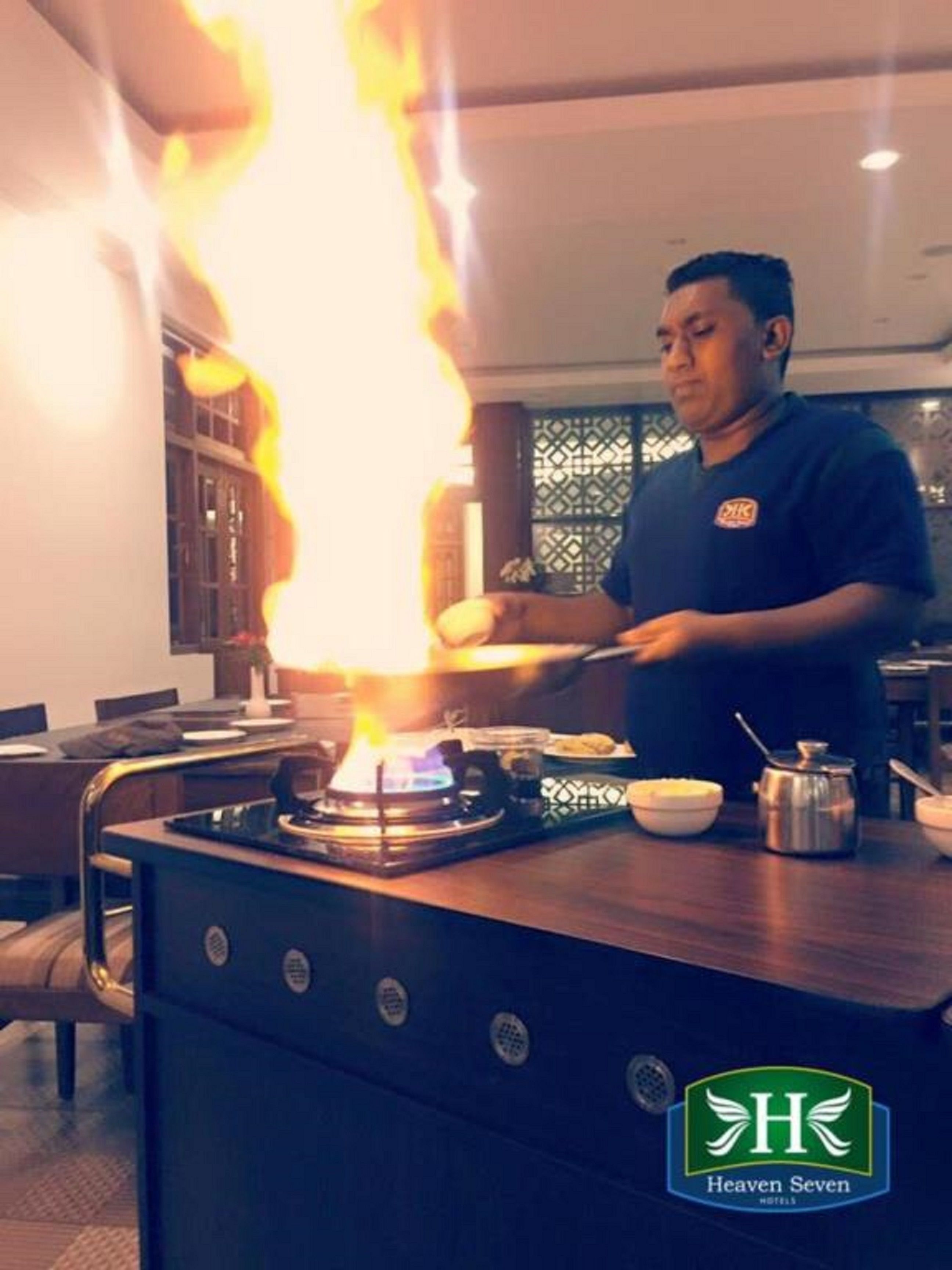 A chef cooking with a large flame on a stove in a restaurant setting.