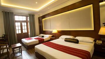 A hotel room with two beds, a wooden headboard, a large window with curtains, a desk, and a chair.