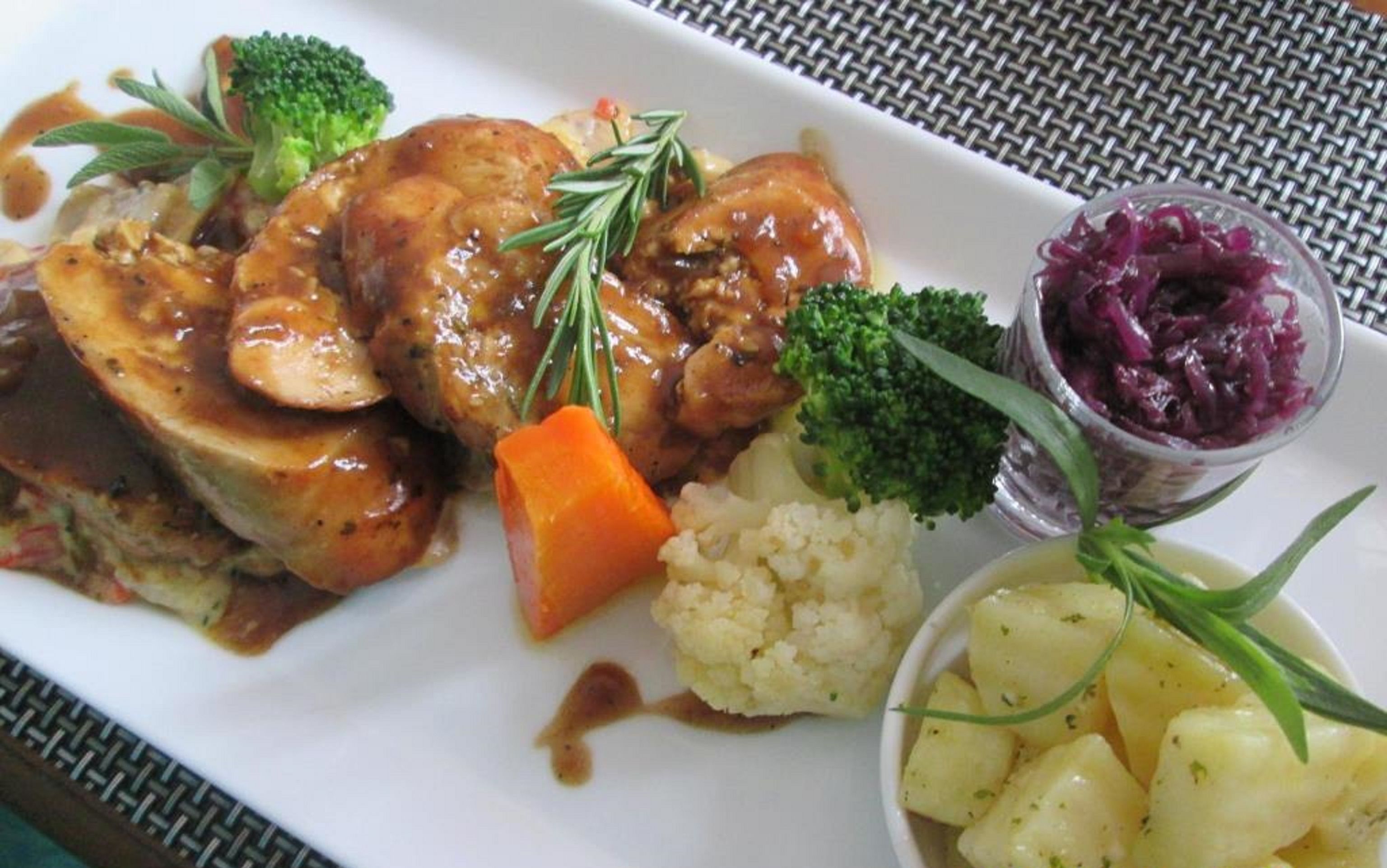 A plate with a meat dish, vegetables, and a small bowl of red cabbage.