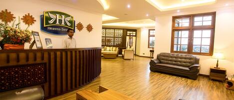 A hotel reception area with a wooden reception desk, leather sofas, and a wooden coffee table.
