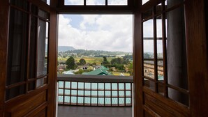 A wooden-framed window with a view of a green-roofed building and a landscape with trees and hills. - Heaven Seven Nuwara Eliya (Nuwara Eliya)