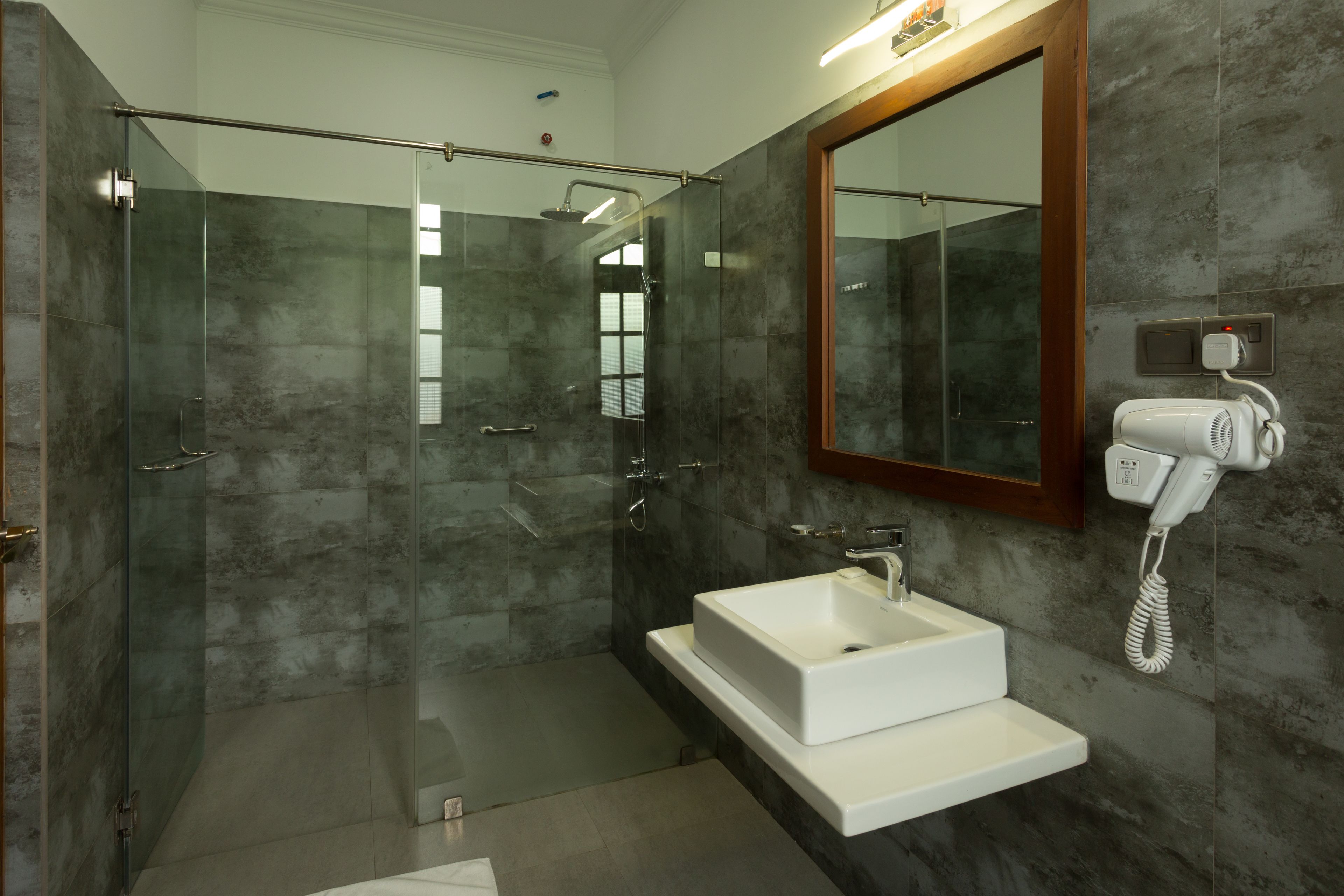 A modern bathroom with a glass-enclosed shower, a white sink, and a hairdryer mounted on the wall.