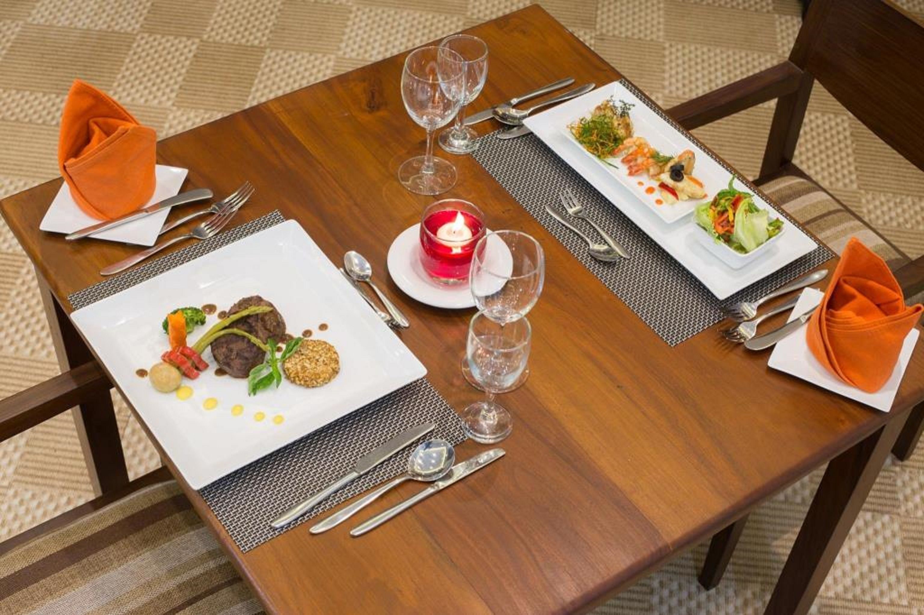 Mesa de comedor dispuesta con dos platos de comida, cubiertos, vasos y una vela encendida.