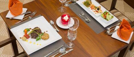 Mesa de comedor dispuesta con dos platos de comida, cubiertos, vasos y una vela encendida.