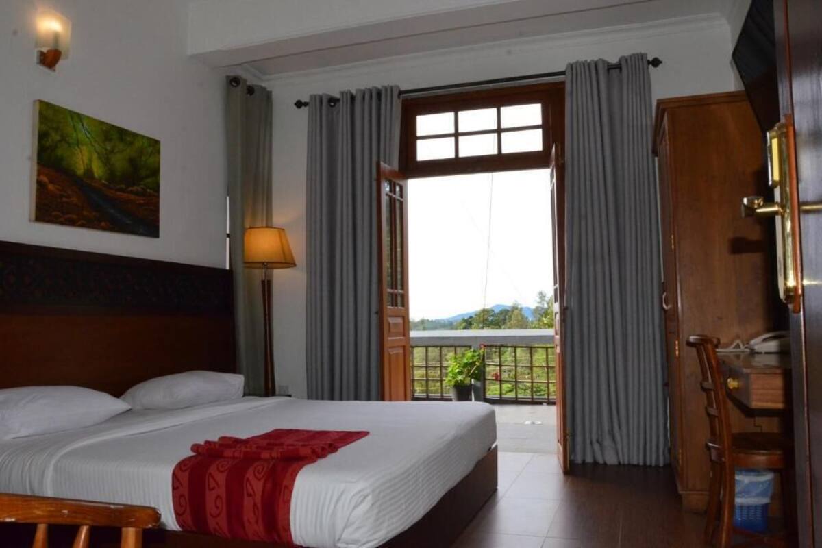 A hotel room with a bed, a desk, a lamp, and a view of the outdoors.