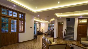 A spacious living area with wooden flooring, a sofa, a coffee table, and a fireplace. There are large windows and a staircase leading to another level. - Heaven Seven Nuwara Eliya (Nuwara Eliya)