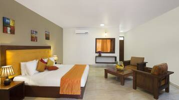 A hotel room with a large bed, a wooden nightstand, a desk, a chair, and a small table with a fruit bowl.