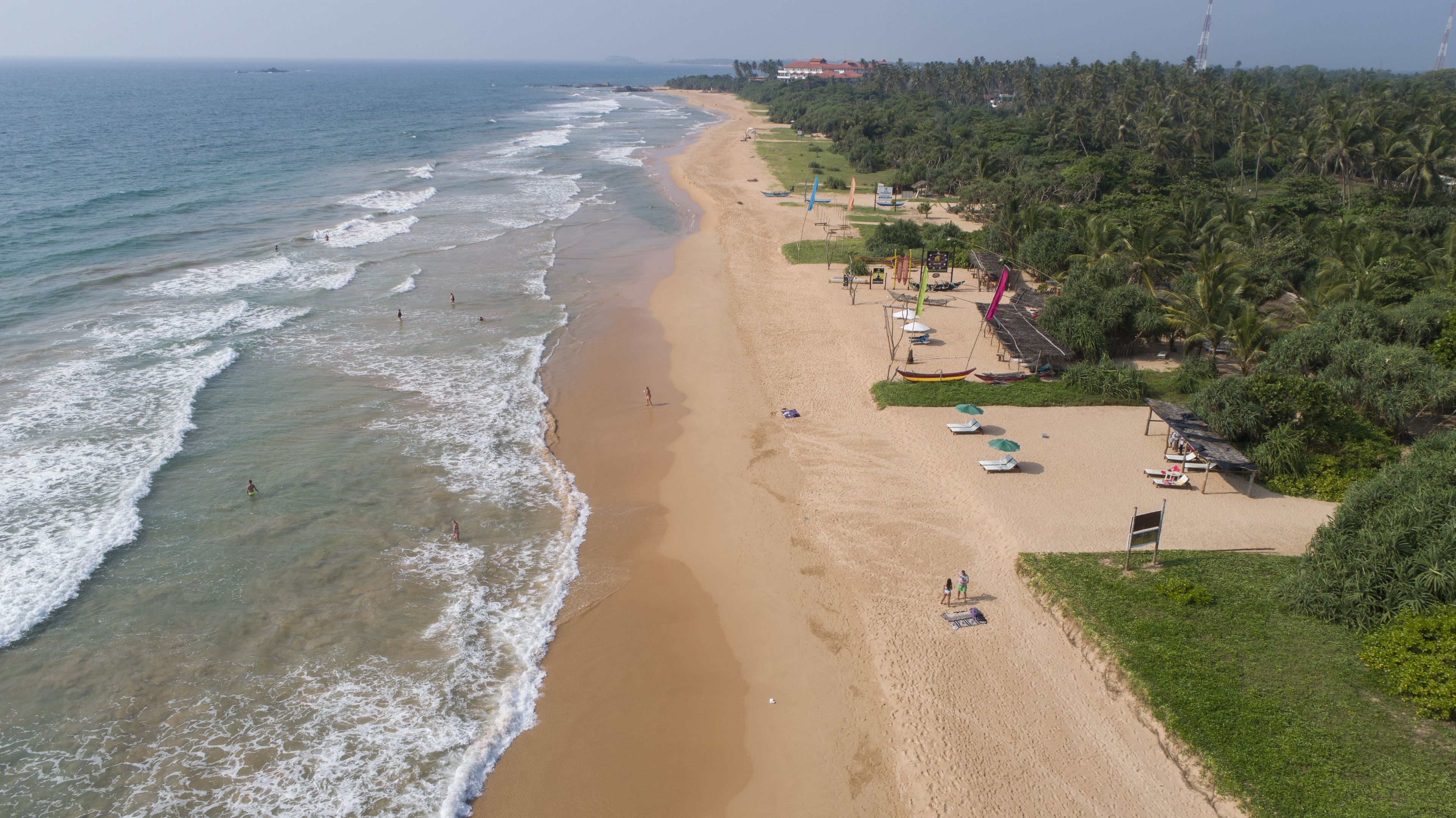 A beach with a long stretch of sand, a few umbrellas, and a few people.