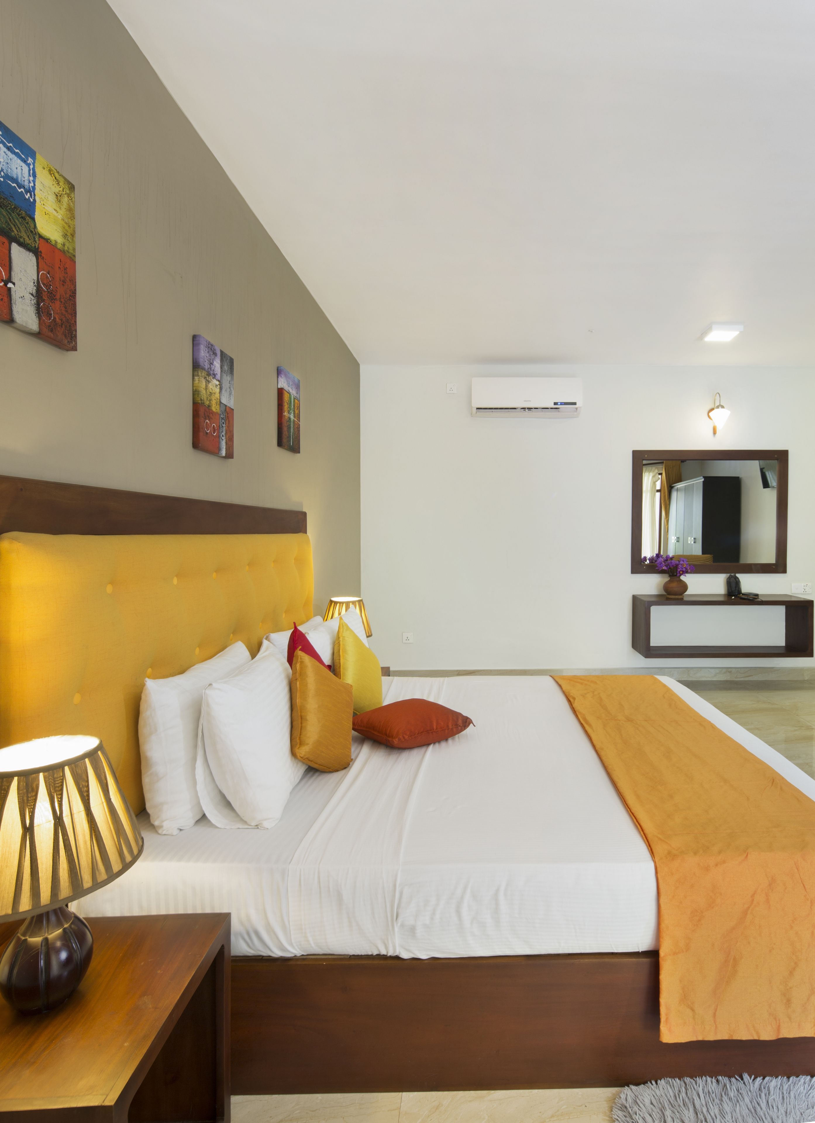 Una habitación de hotel con una cama grande, una lámpara de noche, un espejo y obras de arte en las paredes.