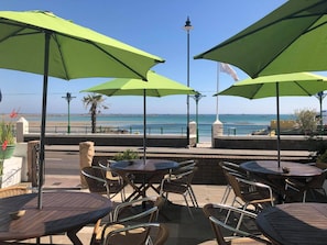 An outdoor seating area with tables and chairs, overlooking a beach. - De L'Etang Jersey (St. Helier)