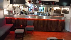 A bar area with a counter, seating, and a television mounted on the wall. - De L'Etang Jersey (St. Helier)