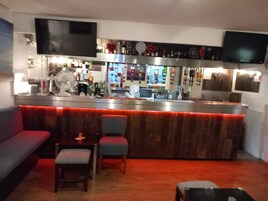 Una zona de bar con mostrador, asientos y un televisor montado en la pared.