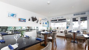 A modern dining area with a black countertop, white plates, and blue napkins. There are multiple dining tables and chairs. - De L'Etang Jersey (St. Helier)