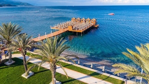 Un resort sobre el agua con un muelle, palmeras y mar azul cristalino.