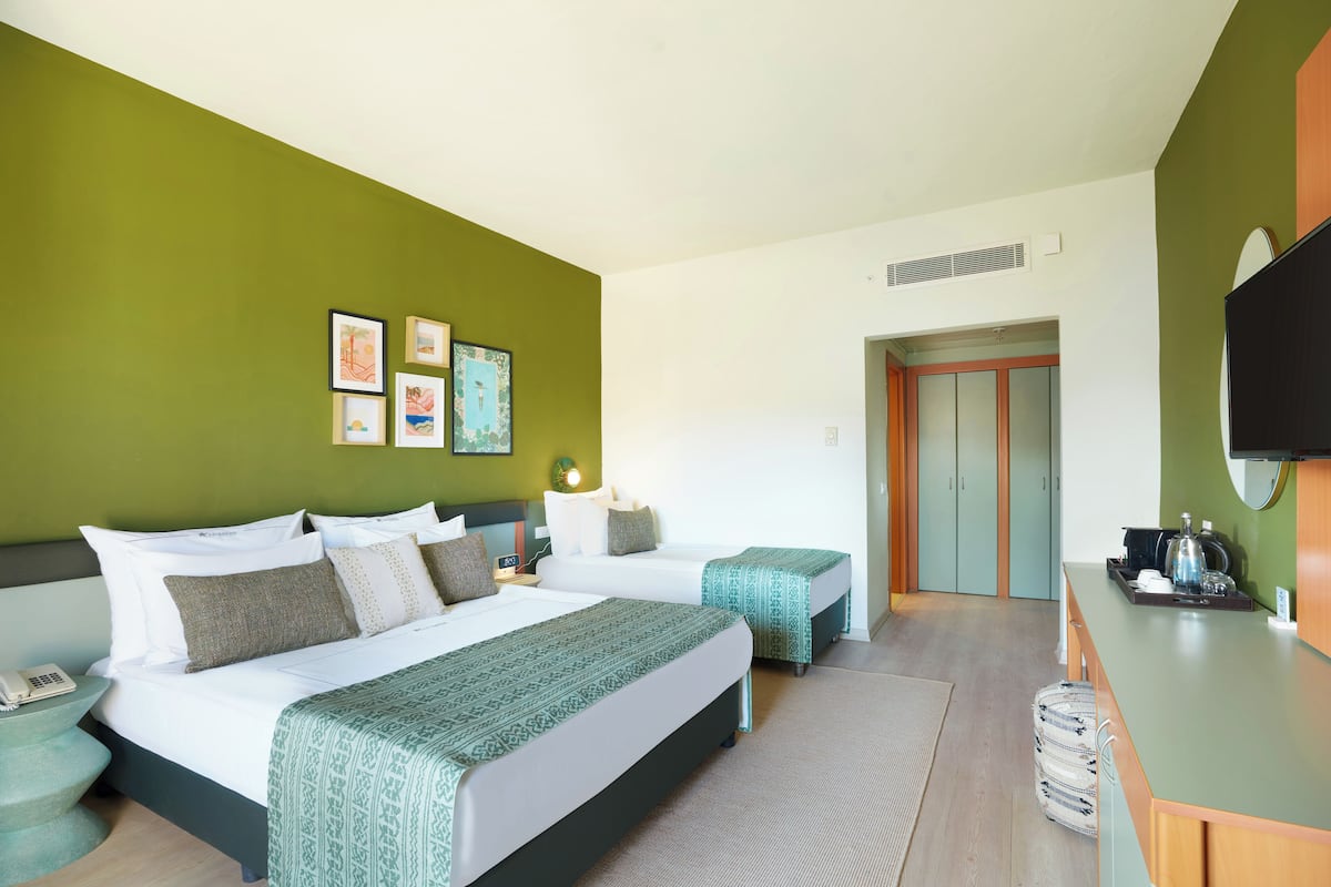 A hotel room with two beds, a desk, a chair, a phone, and artwork on the wall.