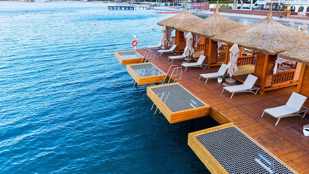 Cabañas sobre el agua con techos de paja, terraza de madera y sillones de descanso.