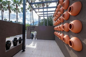 Un patio con macetas de terracota dispuestas en una pared, un pérgola y vistas a palmeras.
