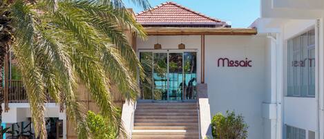 A building with a tiled roof, a staircase leading to a glass door entrance, and a sign reading 'Mesoic.'