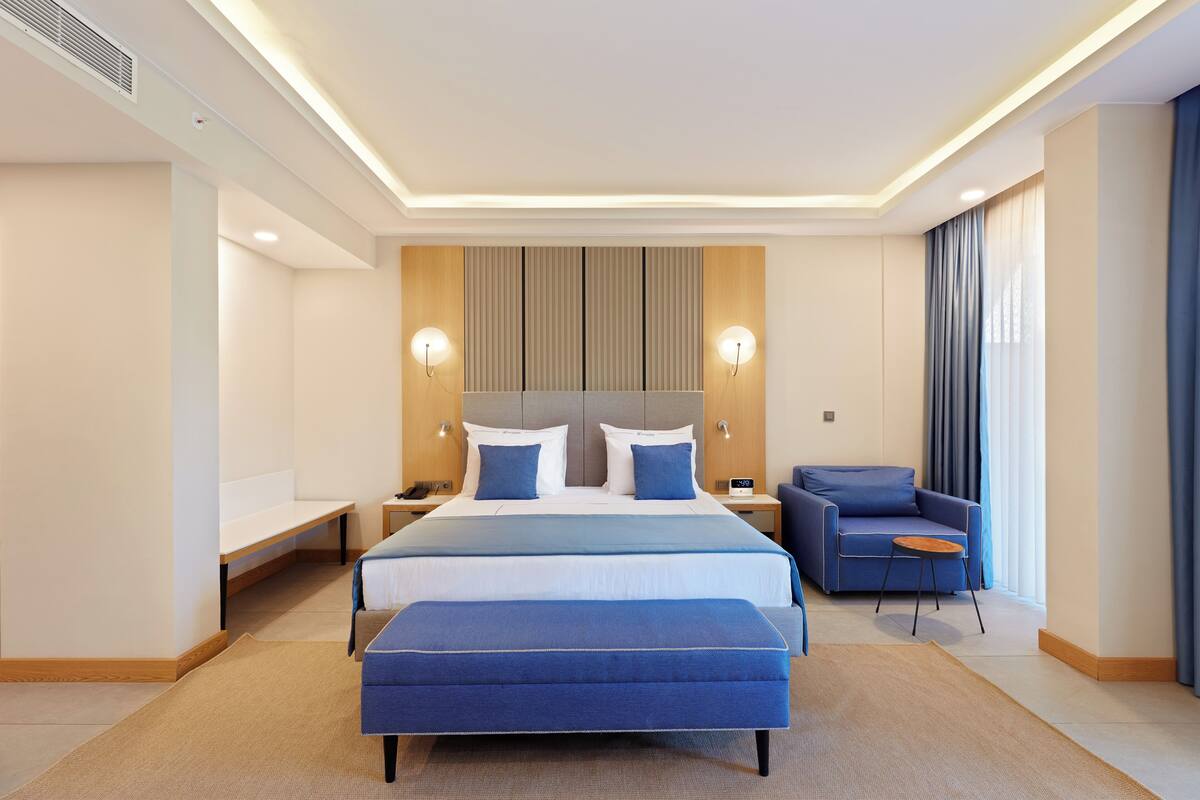 A modern hotel room with a large bed, a sofa, a small table, and a bench.