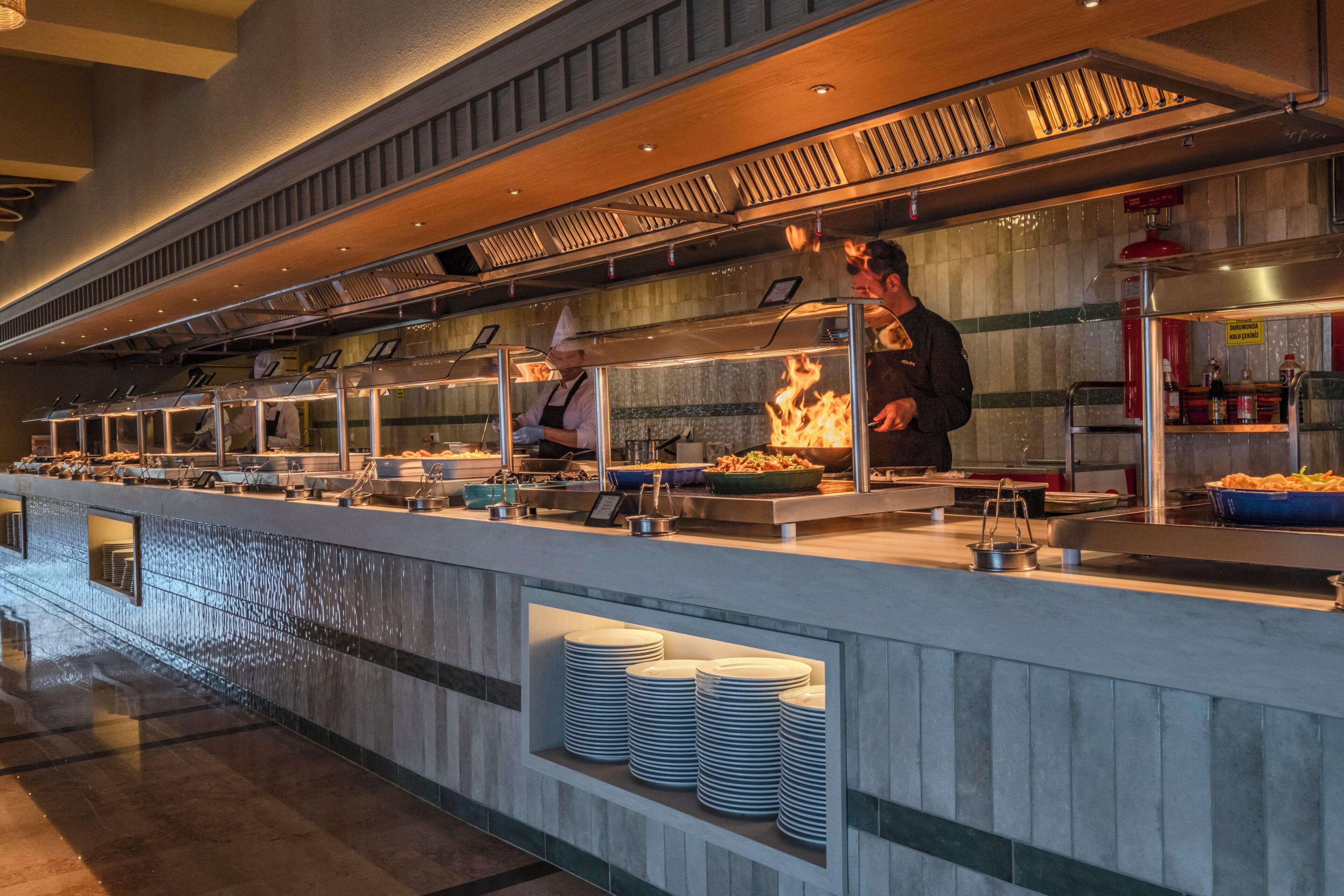 A buffet area with multiple serving stations, a fire feature, and stacked plates.