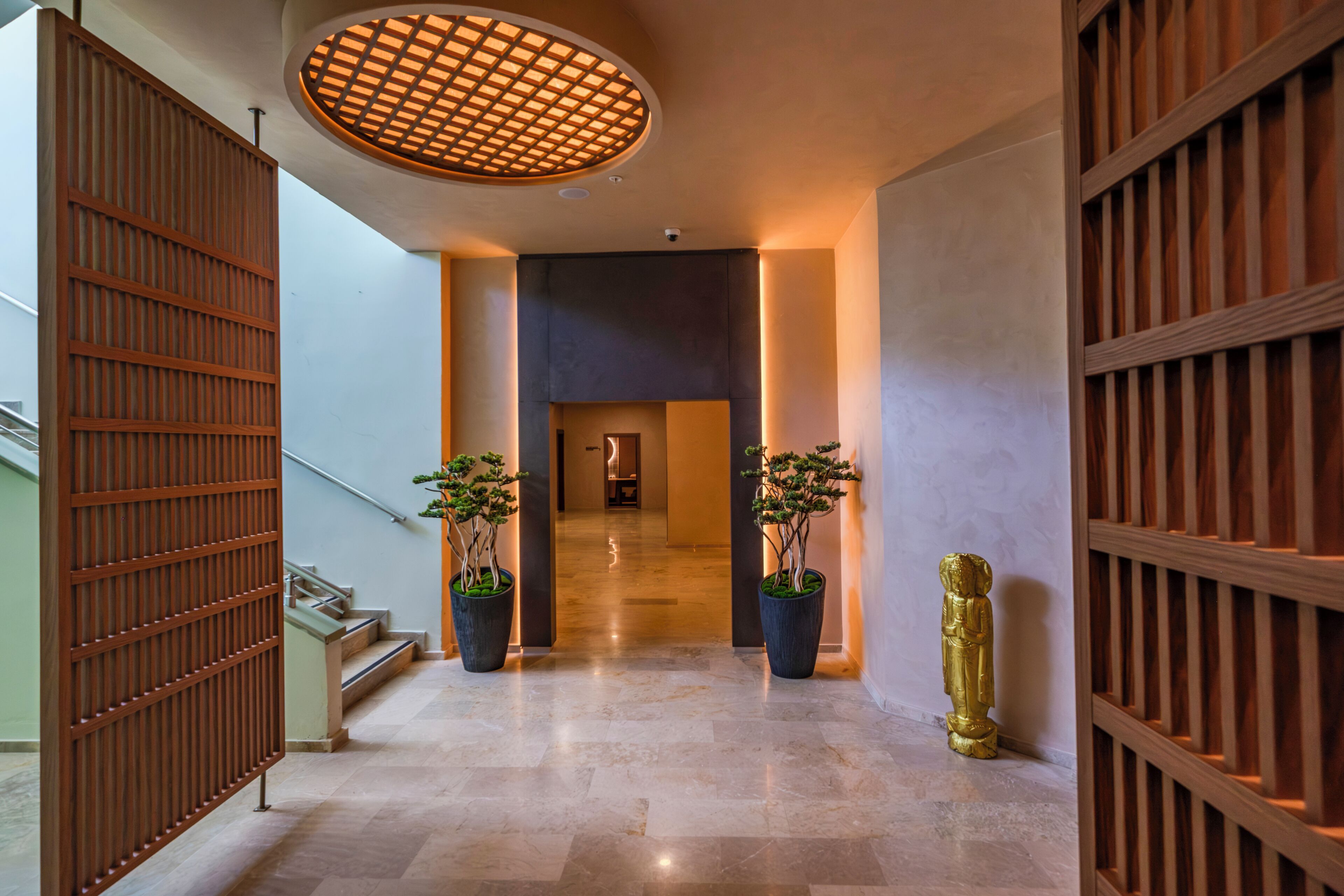 A hallway with a wooden floor, a staircase, and two potted plants.