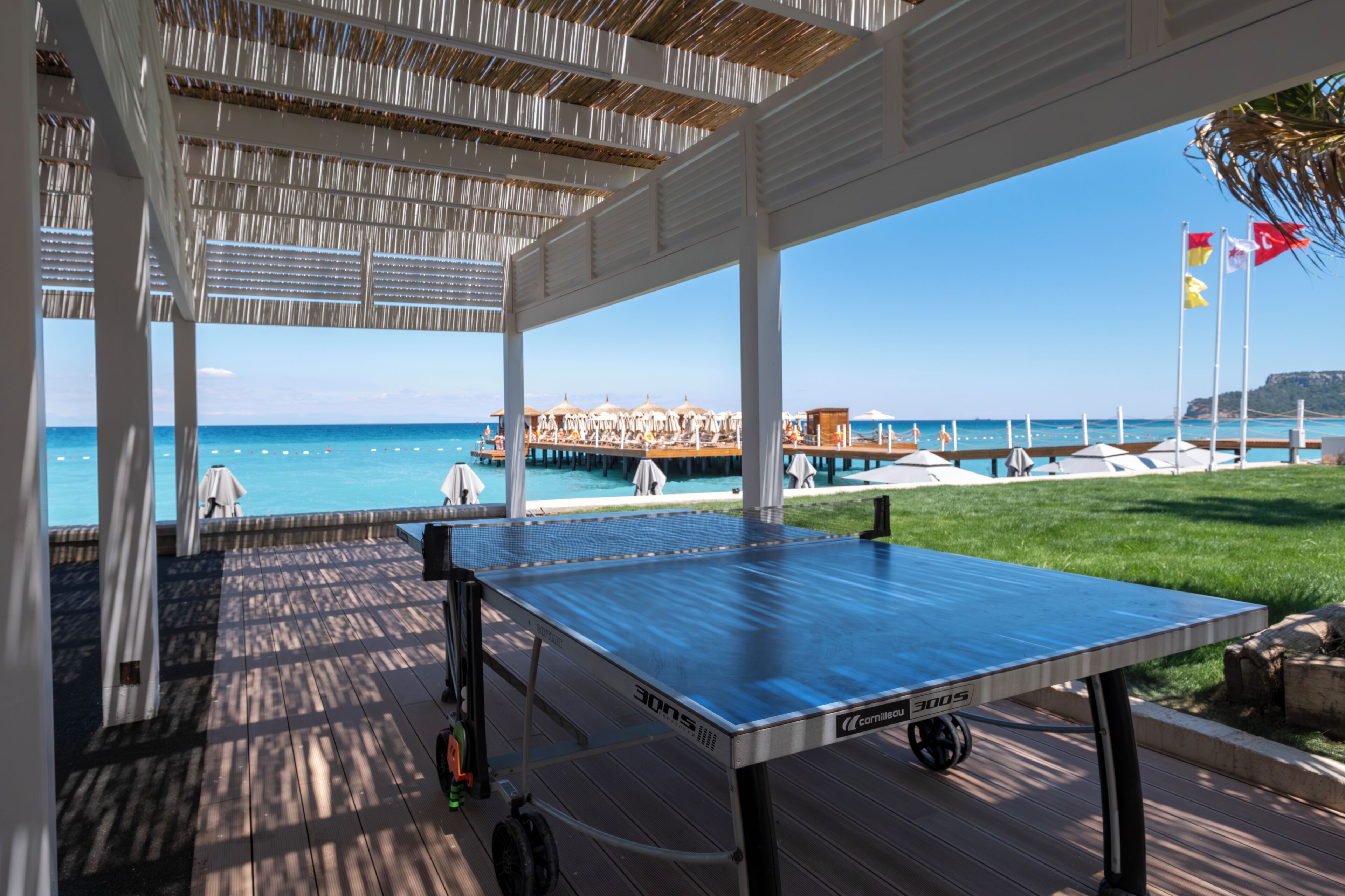 Una mesa de ping pong en un espacio exterior techado con vista al océano y un muelle al fondo.
