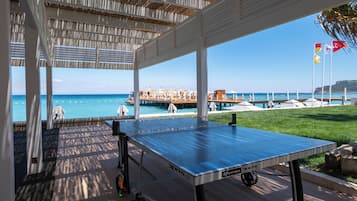 Una mesa de ping pong en un espacio exterior techado con vista al océano y un muelle al fondo.