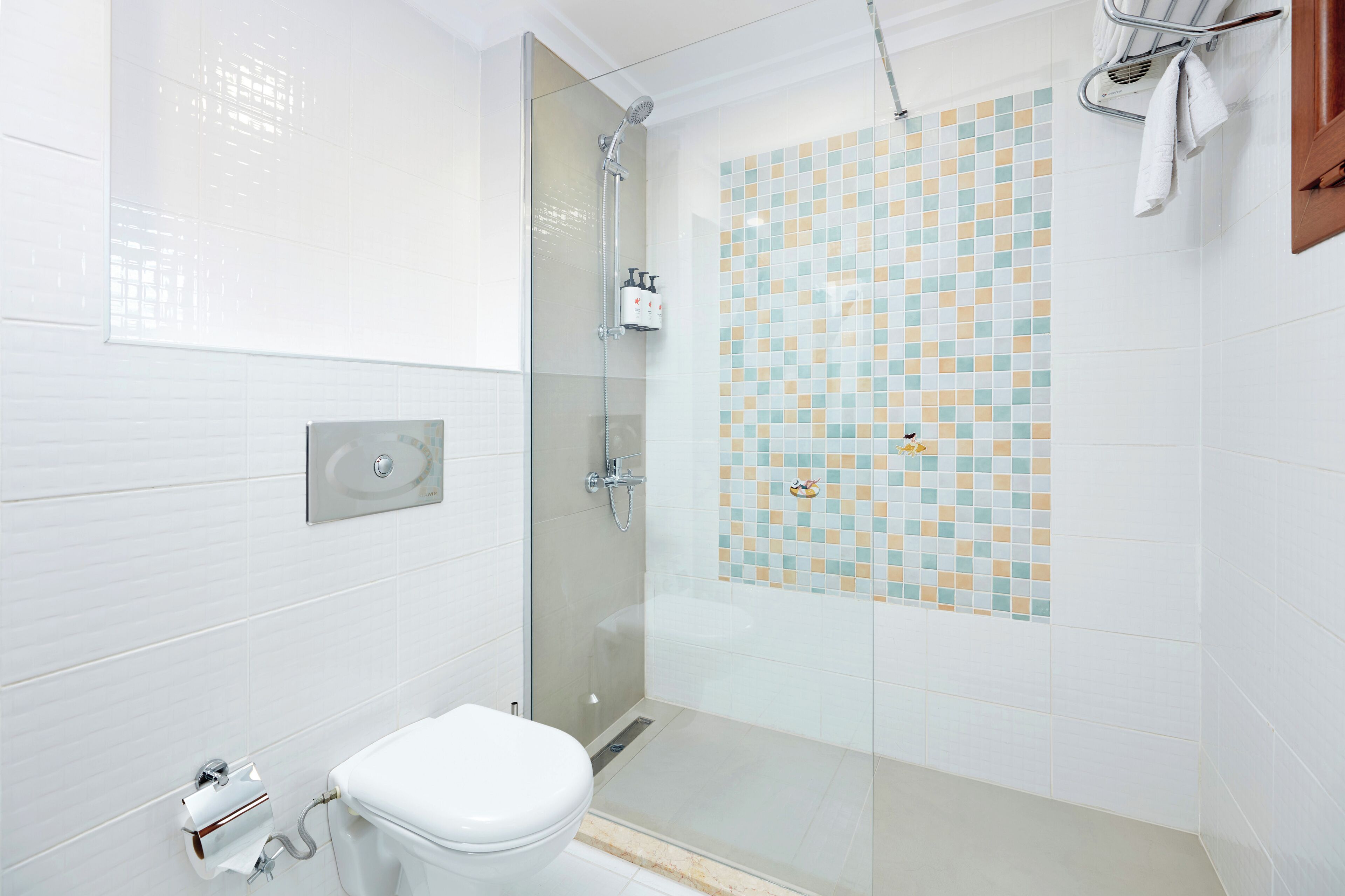 Un baño moderno con ducha envuelta en vidrio, un inodoro y una pared de azulejos con diseño tipo mosaico.