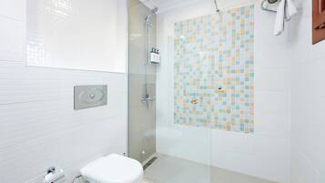 Un baño moderno con ducha envuelta en vidrio, un inodoro y una pared de azulejos con diseño tipo mosaico.