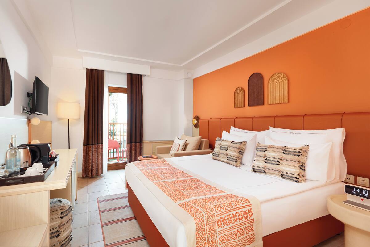 A hotel room with a bed, bedside table, TV, and a desk with a chair.