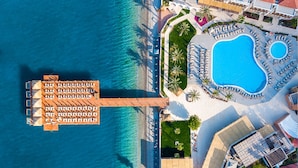 Vista aérea de un complejo turístico con una piscina grande, un área de piscina separada y un muelle con tumbonas.