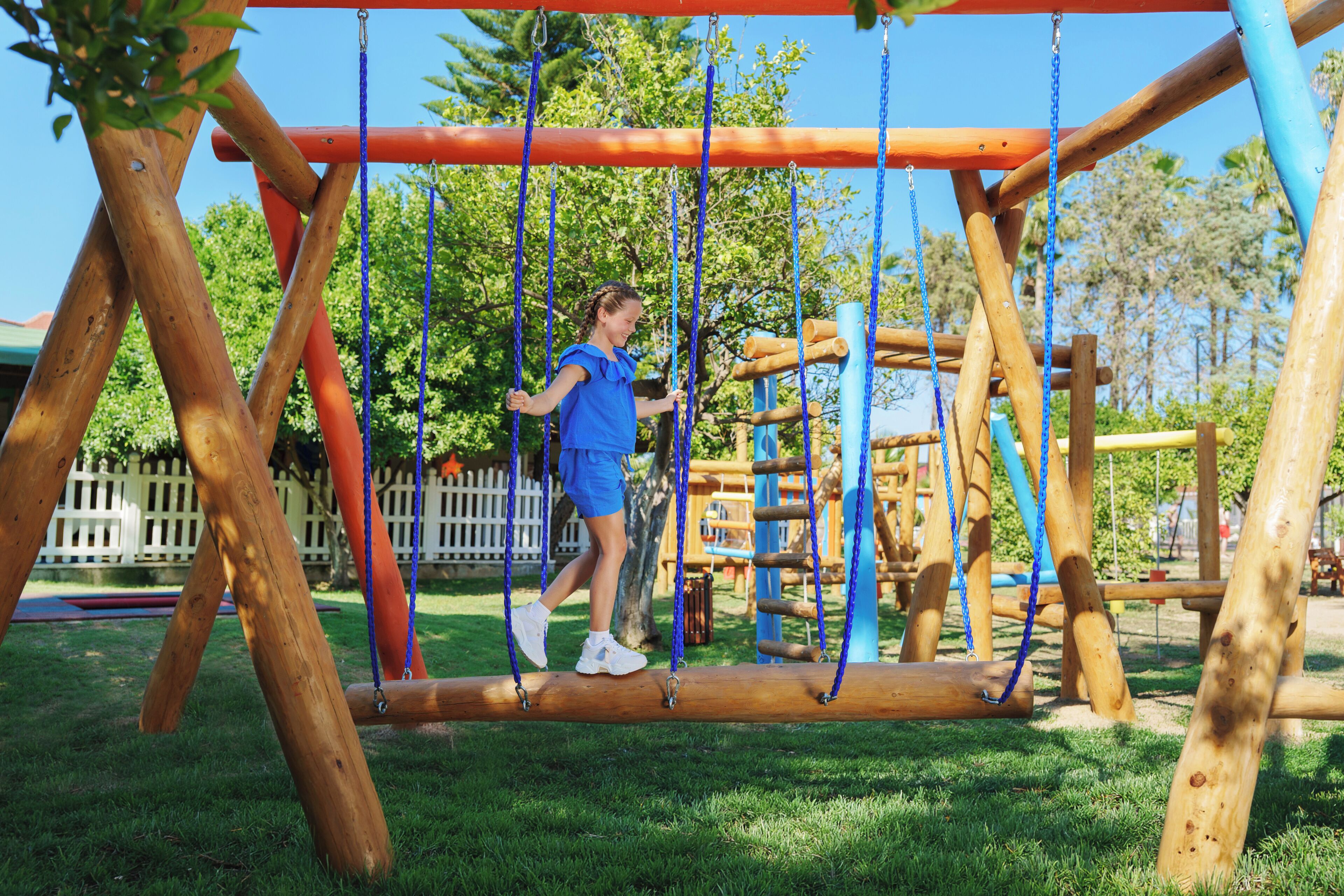 A playground with a wooden swing set and a rope bridge.