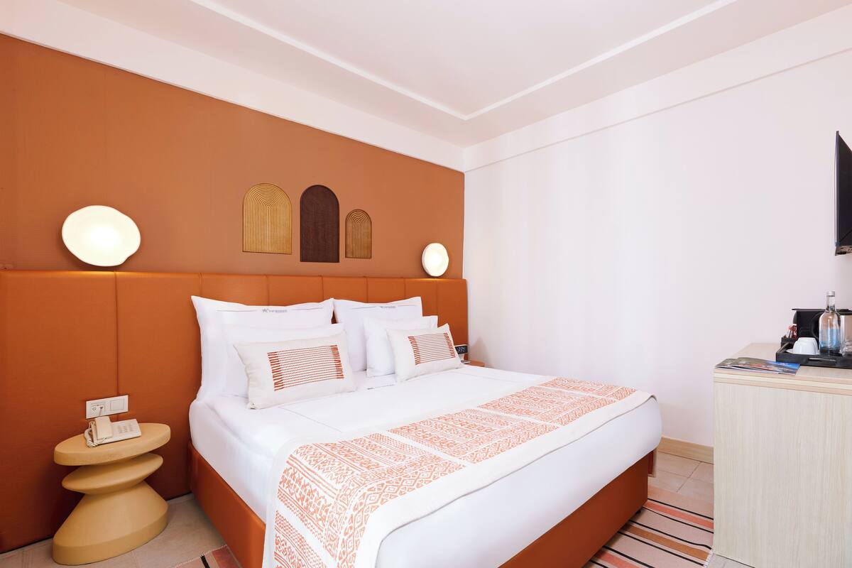 A hotel room with a large bed, a bedside table, a desk, and a wall-mounted TV.